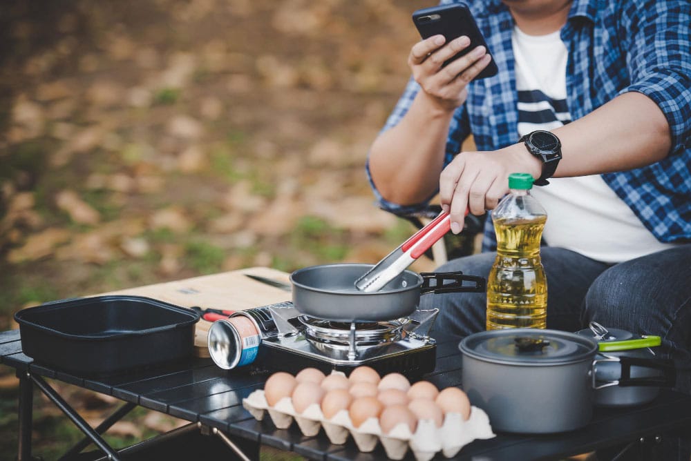 lunettes homme voyageur asiatique frire delicieux oeuf au plat dans poele chaude au camping cuisine plein air voyage camping concept style vie